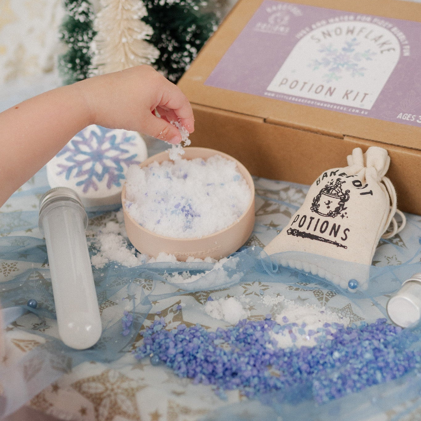 Snowflake potion kit with a hand interacting with a small bowl of snow-like substance, against a decorative background.