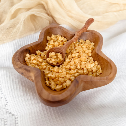 Wooden bowl filled with yellow shimmer rocks and a wooden spoon for nature and water play with children, sensory exploration.