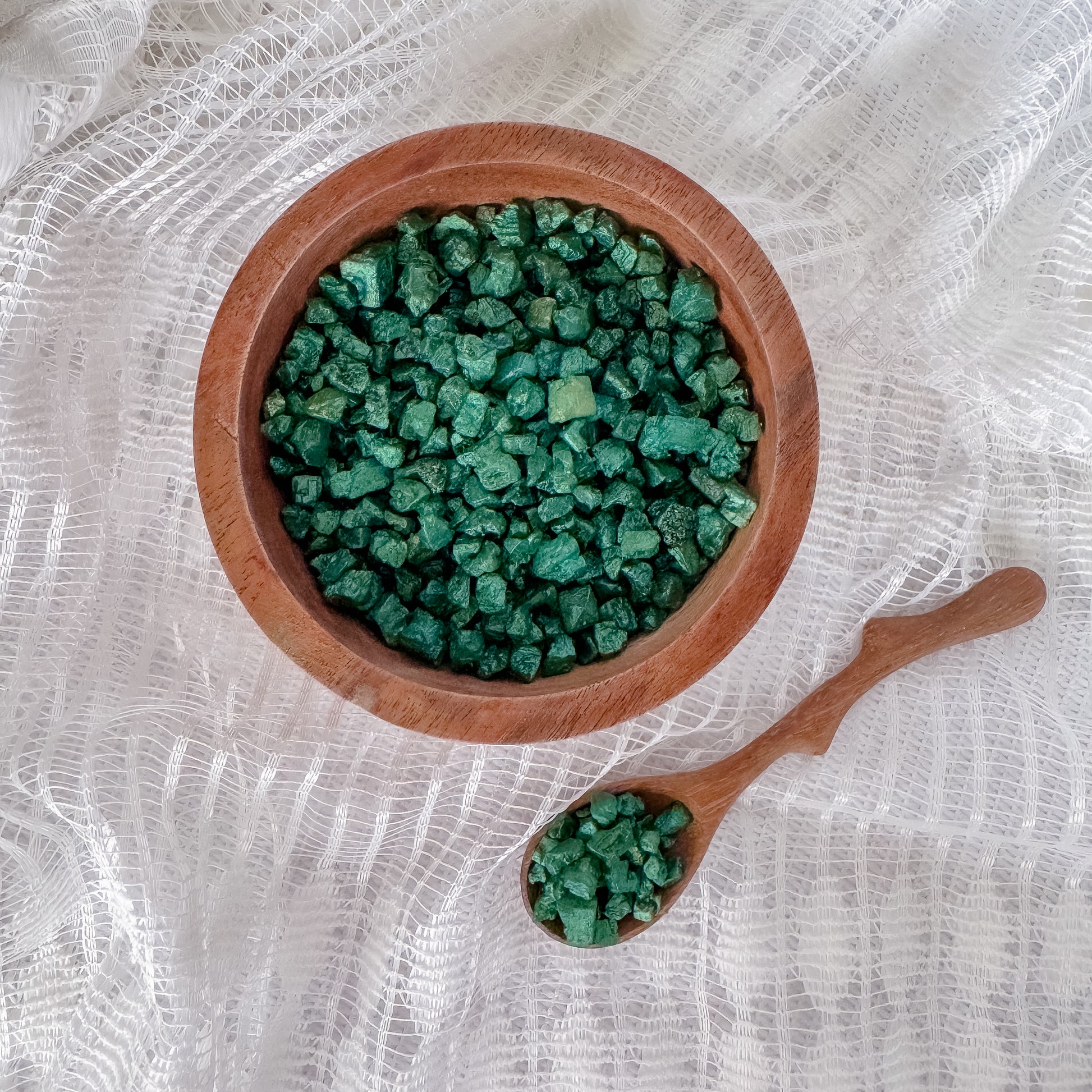 Wooden bowl and spoon filled with green shimmer rocks on a white textured background.