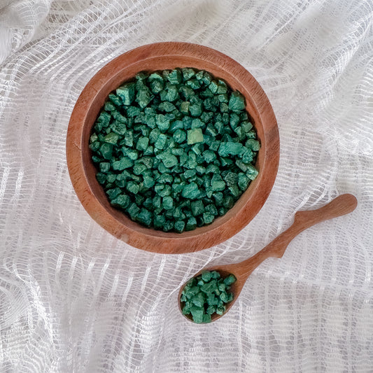 Wooden bowl and spoon filled with green shimmer rocks on a white textured background.