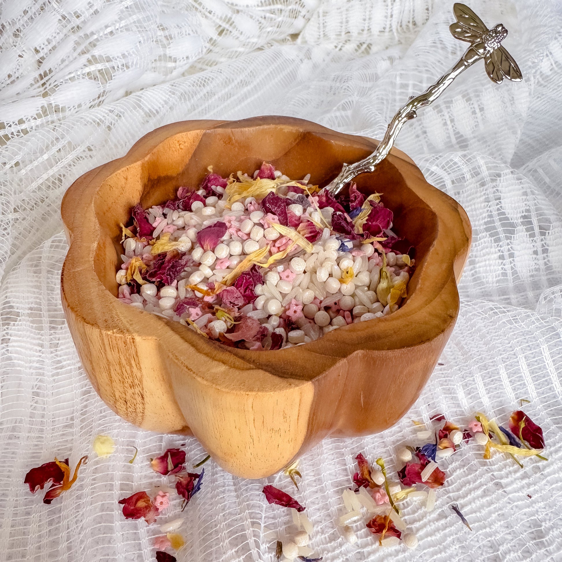 Wooden bowl with sensory rice and dried flowers on a textured white surface. Used for nature and water play with children, sensory exploration.