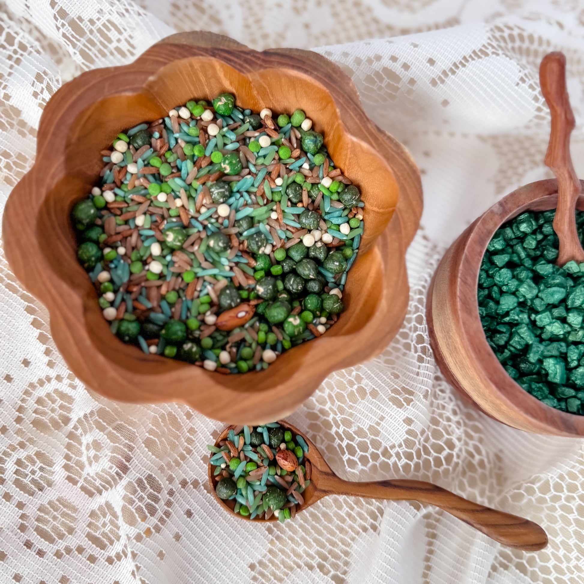 Wooden bowl and spoon filled with green sensory base, rice and grains. Used for nature play with children, sensory exploration.