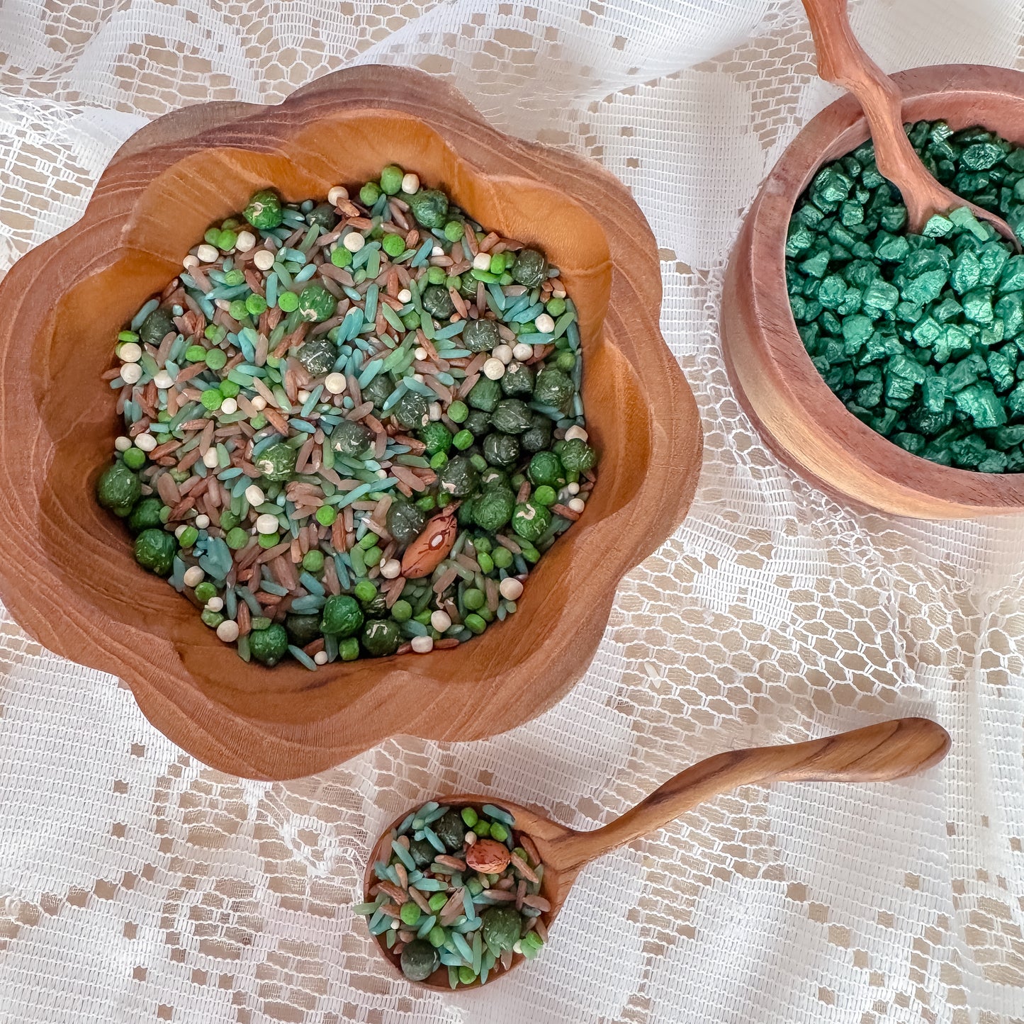 Wooden bowls with green rice and grain sensory base and a wooden spoon on a lace tablecloth