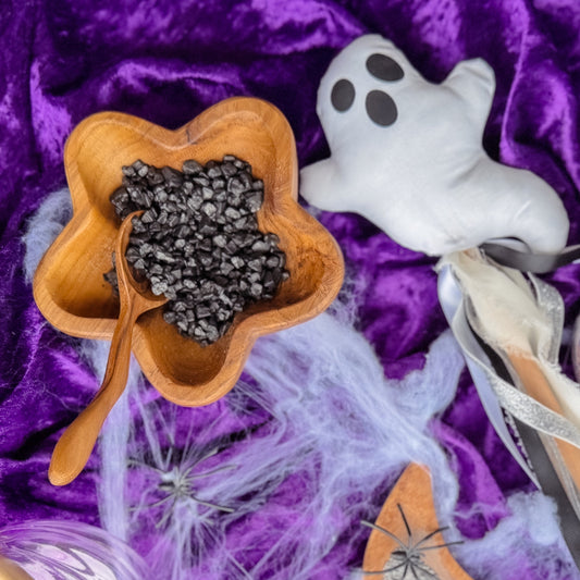 Halloween-themed items including a ghost, spider, and decorative elements on a purple fabric background.  Wooden star bowl of black shimmer rocks for nature and water play with children, sensory exploration.