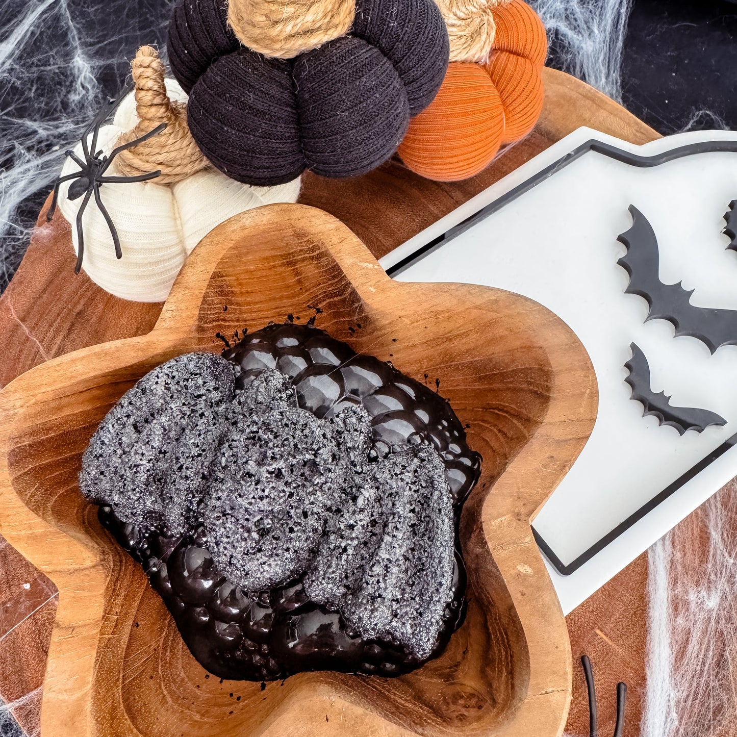 Black bat fizzer with bubbles in a wooden bowl with Halloween-themed decorations. Children sensory play