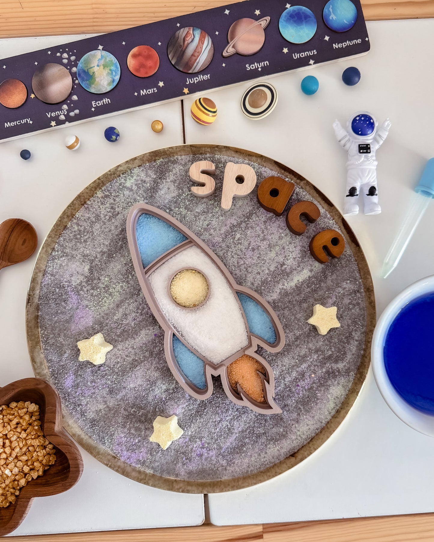 Sensory play set up with space-themed design including a rocket ship, planets, and stars on a white surface.