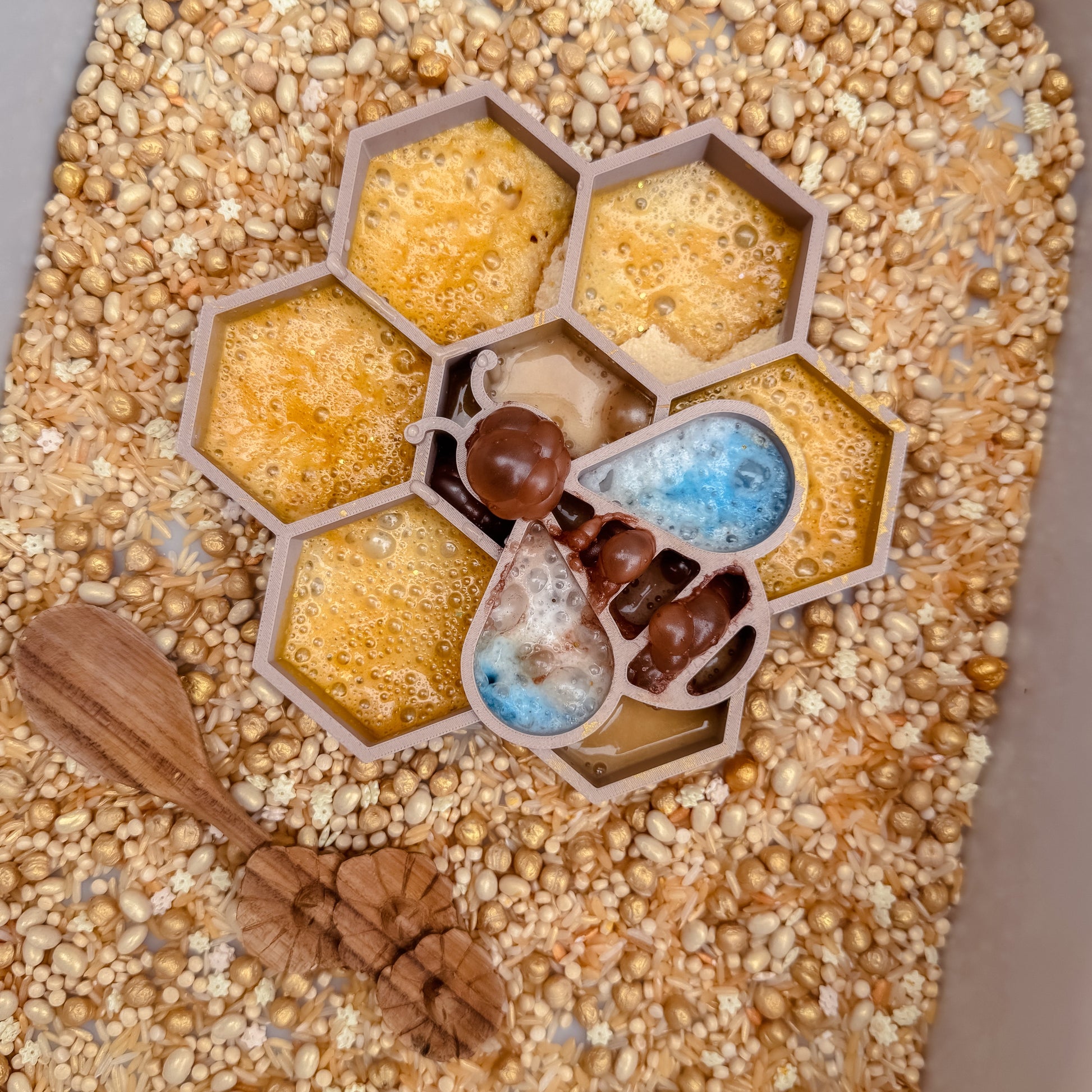 Honeycomb-shaped sensory tray with bee, wood spoon and golden sensory base and fizz