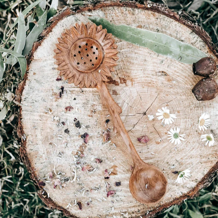 Wooden flower shaped spoon and sifter on a tree stump with greenery