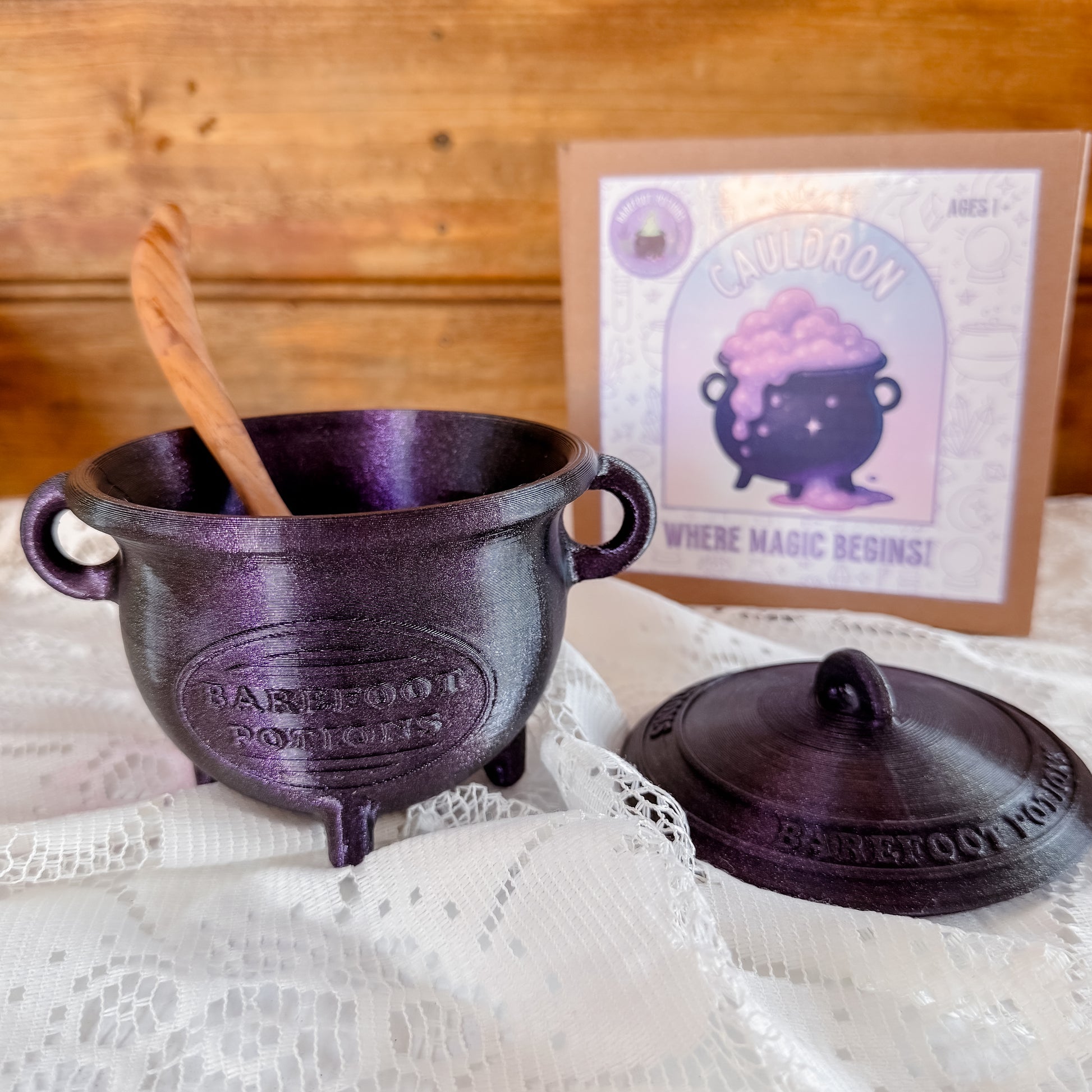 Glittery purple cauldron with wooden spoon on a lace tablecloth, 3D printed for children sensory potion play