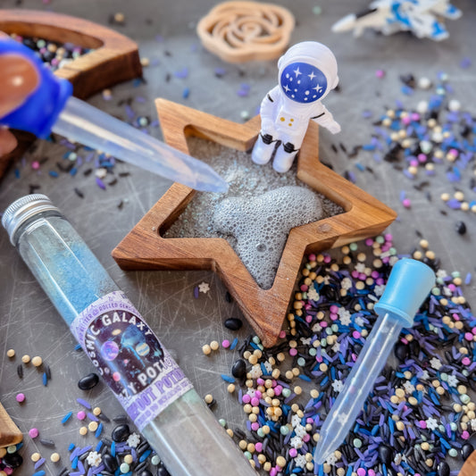 Space-themed setup with star-shaped wooden container, astronaut figurine, and colorful sprinkles on a gray surface.
