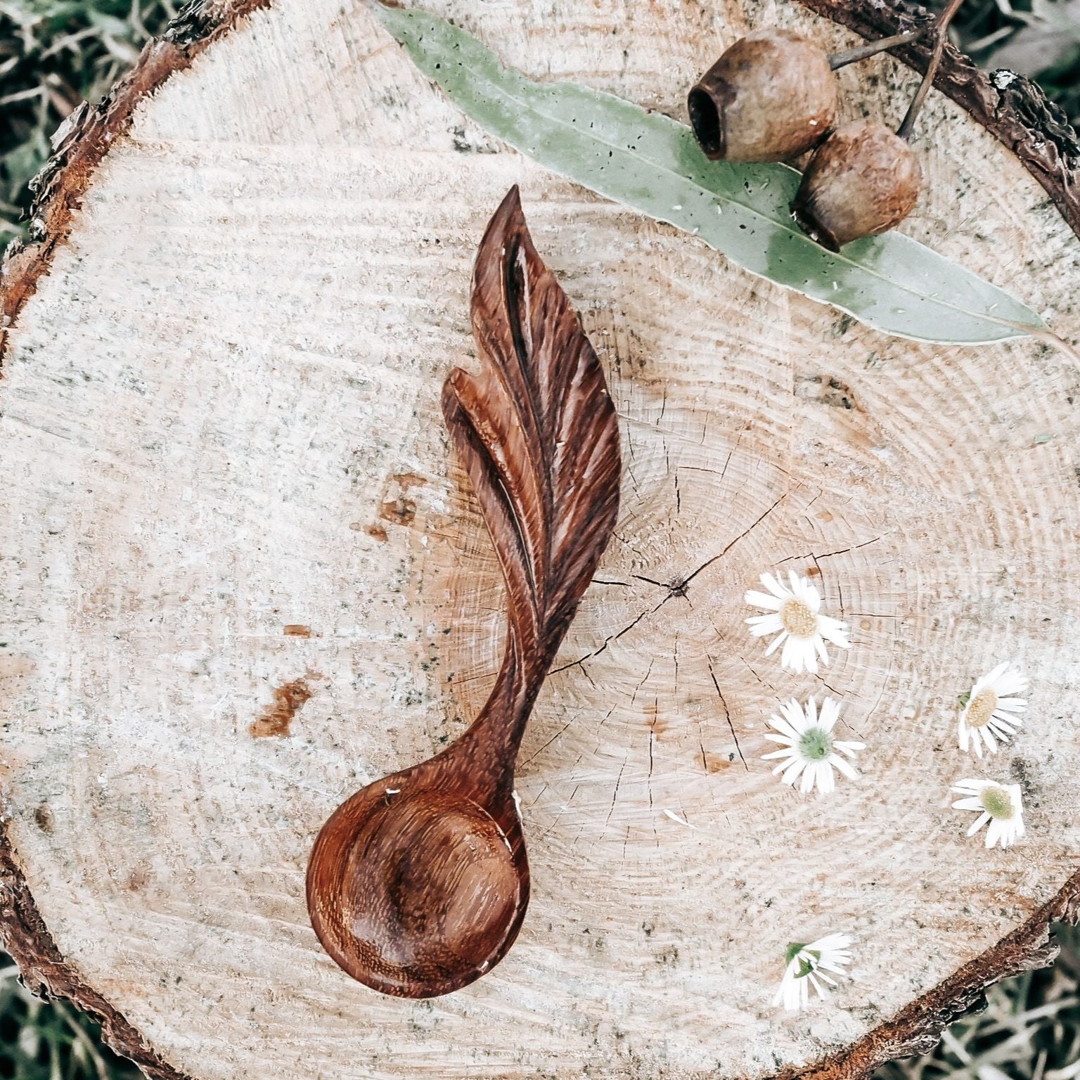 Wooden leaf-shaped spoon on a wooden log with acorns and flowers