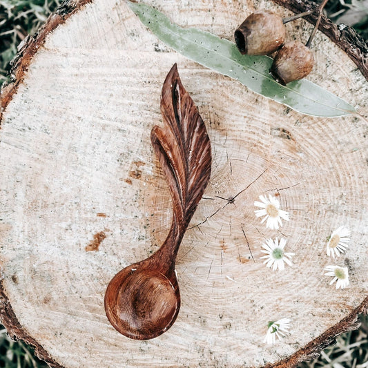 Wooden leaf-shaped spoon on a wooden log with acorns and flowers