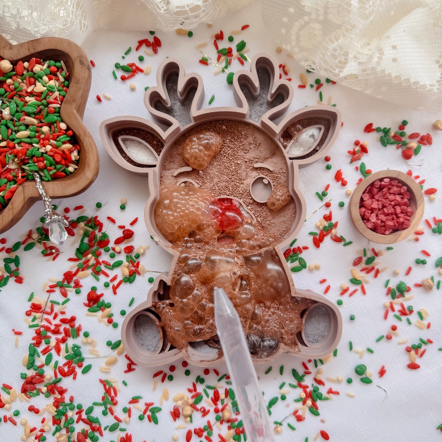 Reindeer-shaped sensory tray with fizz on a white surface surrounded by colorful sprinkles.