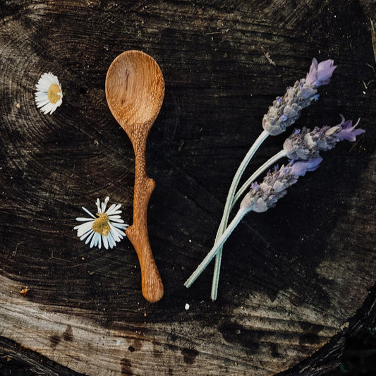 Wooden spoon on a dark wooden surface with lavender and daisies.