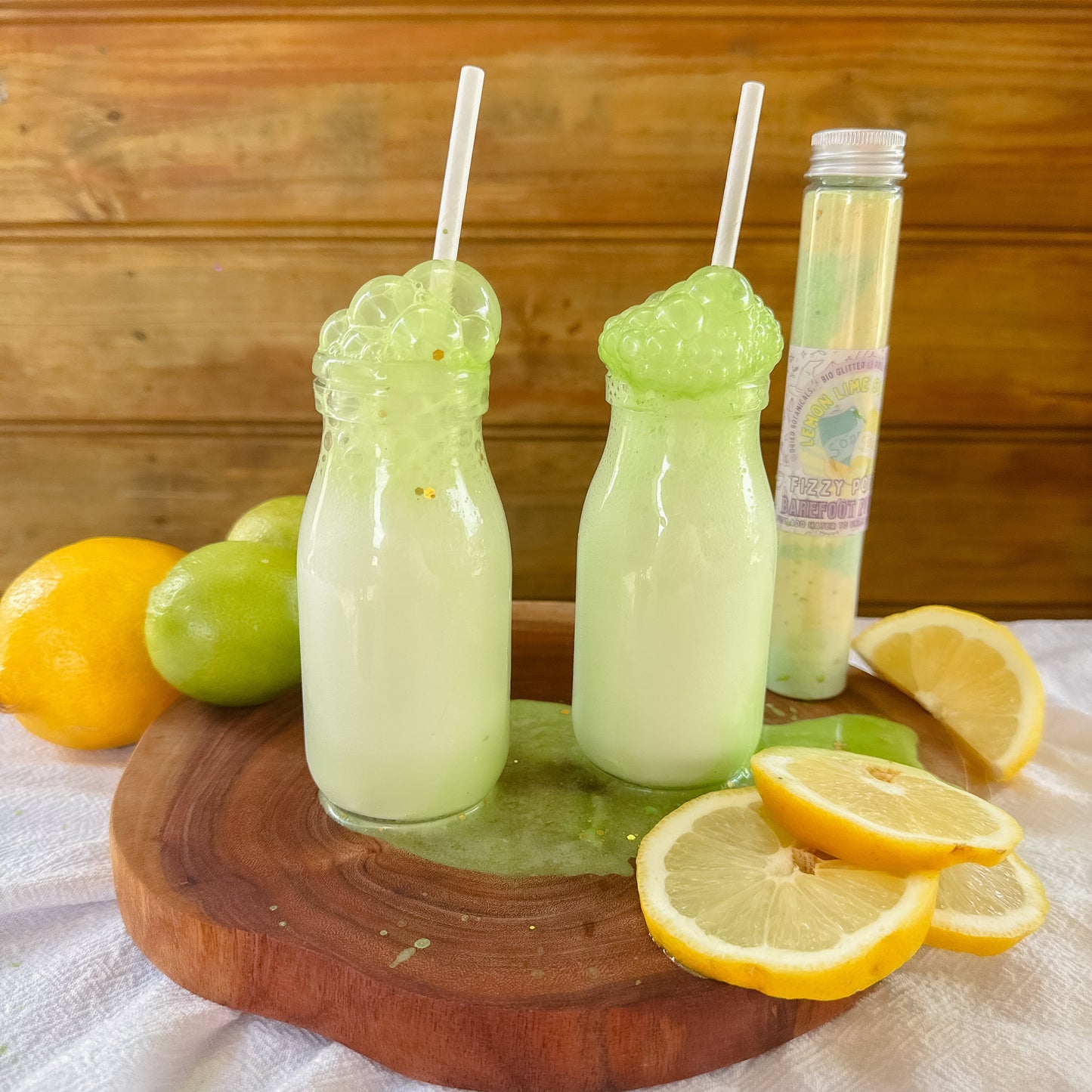 Two glass bottles with green liquid on a wooden board with lemons and limes.